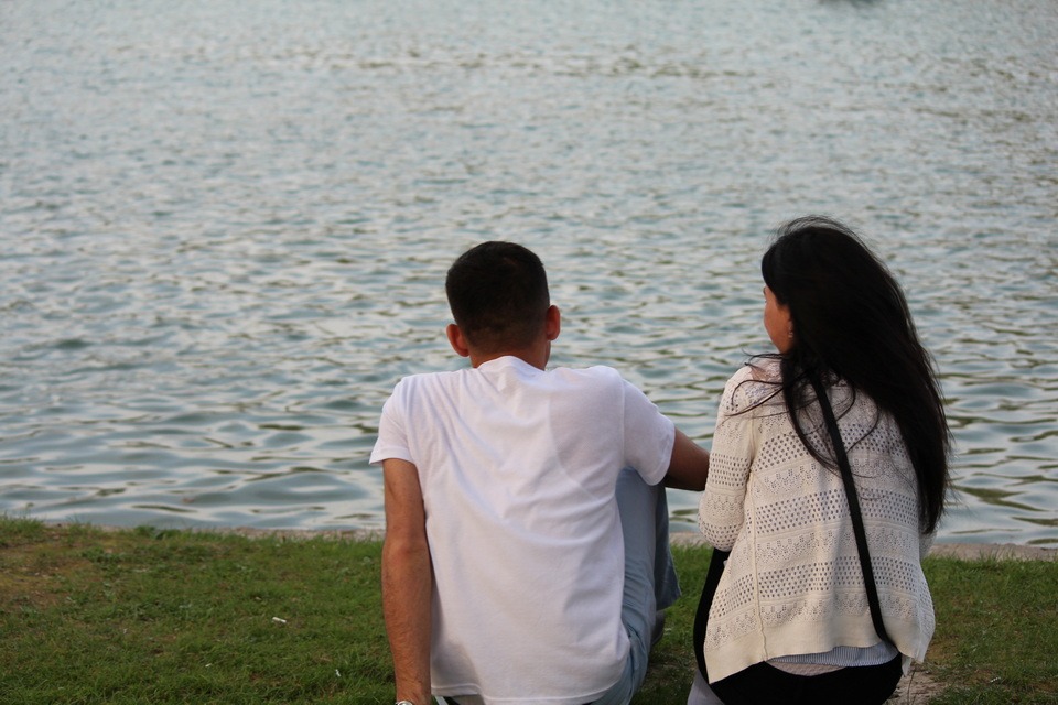 A picture of a man and a woman sitting on grass and looking out over water